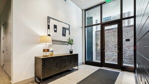Een moderne lobby met een houten console, een vloerlamp en een potplant.