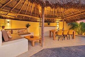 Een terras met rieten dak, een bank, een tafel en stoelen.
