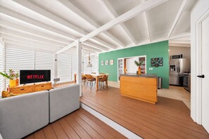 Ein moderner Wohnraum mit Flachbildfernseher, Holzboden, Essbereich und einer Küche mit Edelstahlgeräten.