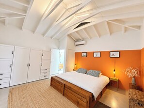 Ein Schlafzimmer mit schrägen Wänden, einem Bett mit weißer Bettdecke, einem Holz-Kopfstück und einem Nachttisch mit Lampe.