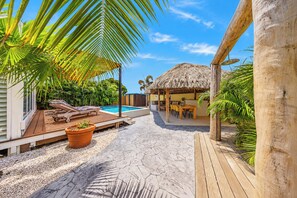 Ein Poolbereich mit Liegestühlen, einer Struktur mit Reetdach und einem Esstisch.