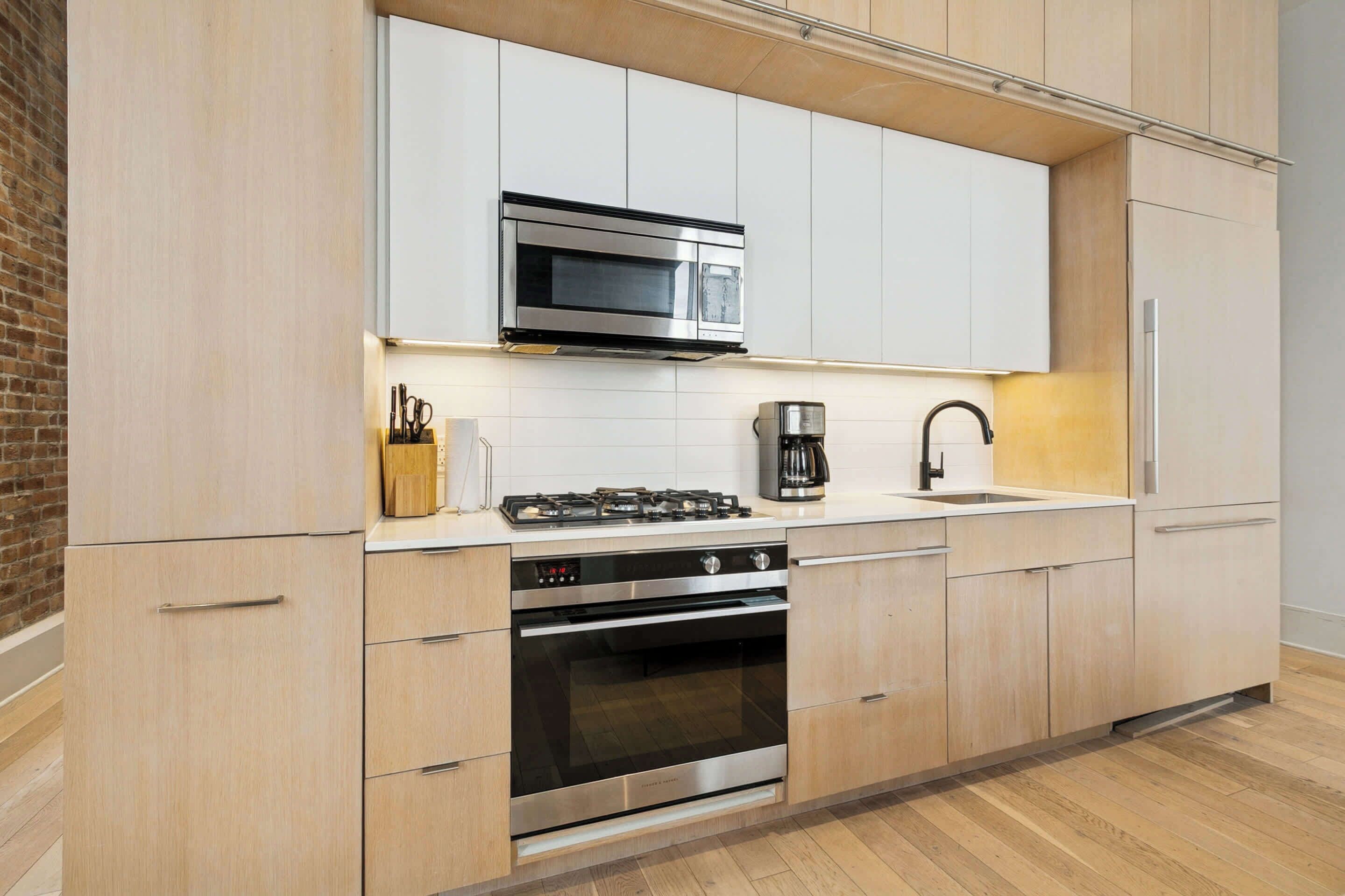 A modern kitchen with white cabinets, a stainless steel microwave, a gas stove, and a built-in oven.