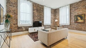 Un soggiorno moderno con pareti in mattoni a vista, un'ampia finestra, una TV a schermo piatto, un divano e un'area pranzo.
