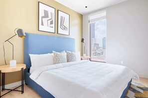 Une chambre d’hôtel moderne dotée d’un grand lit, d’une table de chevet, d’un bureau et d’une fenêtre donnant sur la ville.