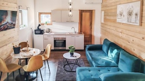 Ein kompakter Wohnbereich mit Küchenzeile, einem Essbereich mit Tisch und Stühlen sowie einem blauen Sofa.