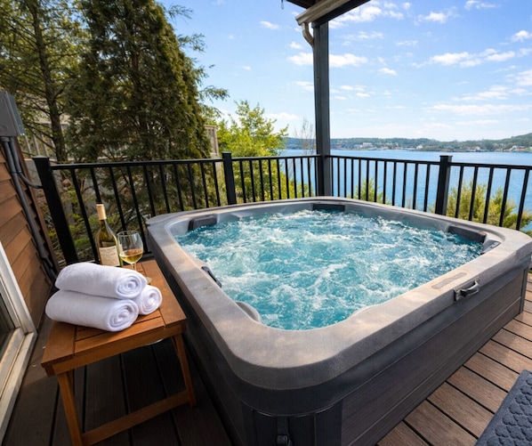 Un bain à remous sur une terrasse en bois, avec vue sur un lac et des arbres.
