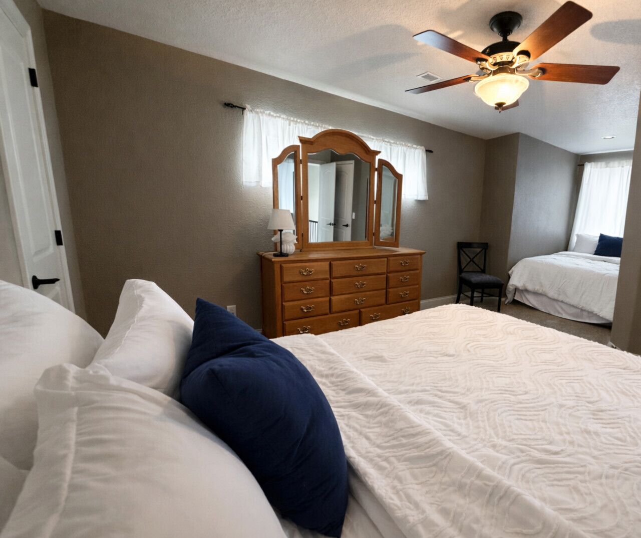 Quarto com cama, penteadeira, espelho e ventilador de teto.