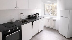 A modern kitchen with white cabinets, a black countertop, a built-in oven, and a window with a view of trees. - Living on the Rhine: Central, spacious & by the cathedral! (Köln)