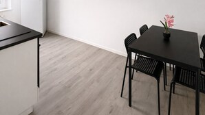 A modern kitchen with white cabinets and a black countertop. There is a dining area with a black table and chairs, and a small potted plant on the table. - Living on the Rhine: Central, spacious & by the cathedral! (Köln)