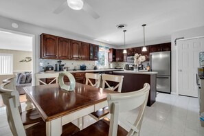 A modern kitchen with dark wooden cabinets, a stainless steel refrigerator, and a dining area with a wooden table and white chairs.