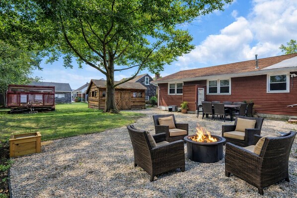 A backyard with a fire pit, wicker furniture, and a wooden structure.