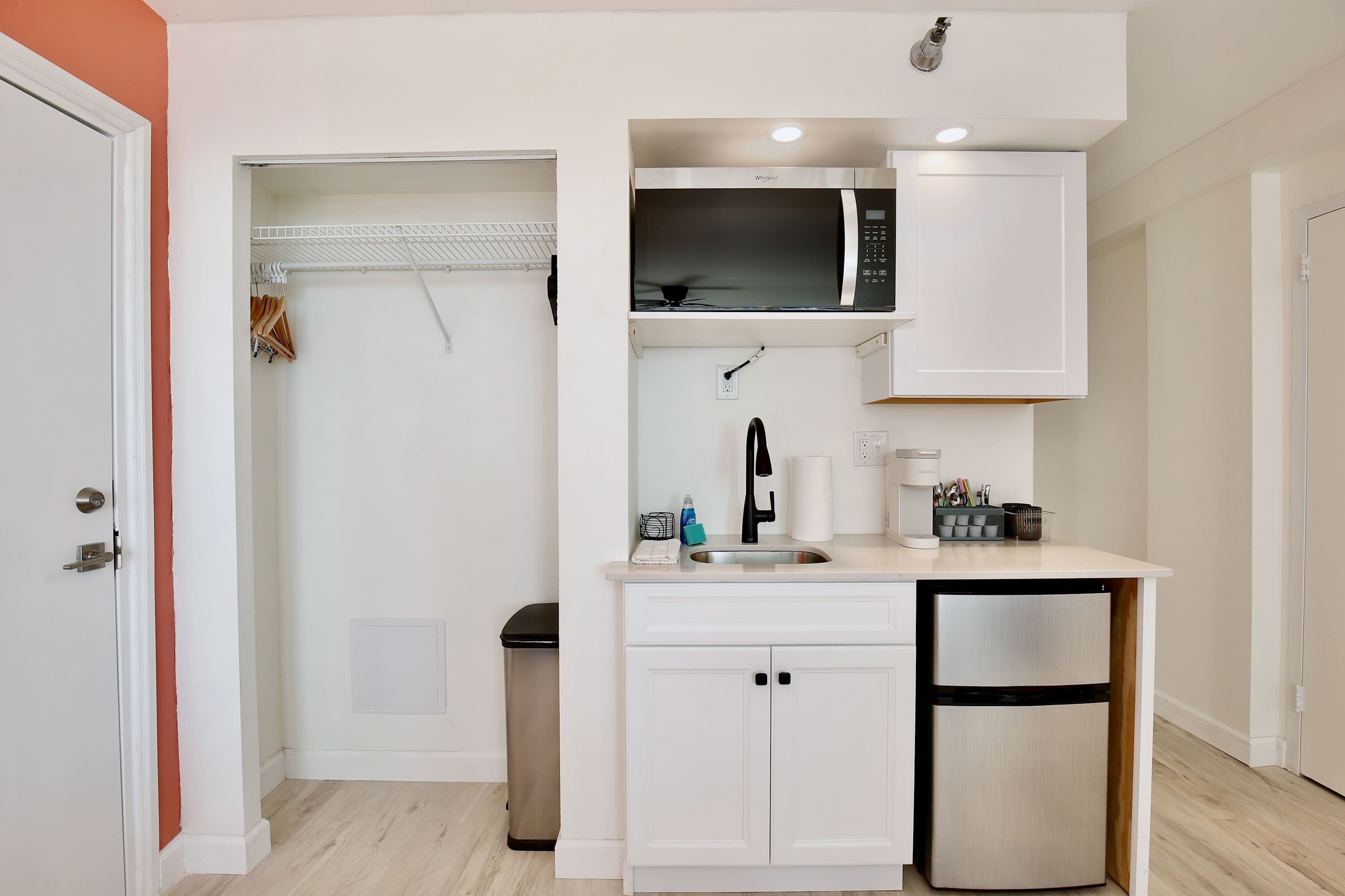 A compact kitchen with a microwave, sink, and refrigerator, featuring white cabinetry and a small countertop.