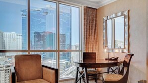 A hotel room with a large window, a round table, a chair, a lamp, and a mirror. - 12th Flr Panoramic Strip View| King Bed + Jacuzzi (Las Vegas)
