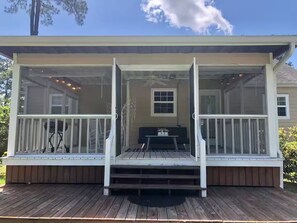 A covered porch with a wooden deck, white railings, and a small table with chairs.