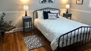 Un dormitorio con cama, dos mesitas de noche con lámparas, un tapete estampado y cuadros en la pared.