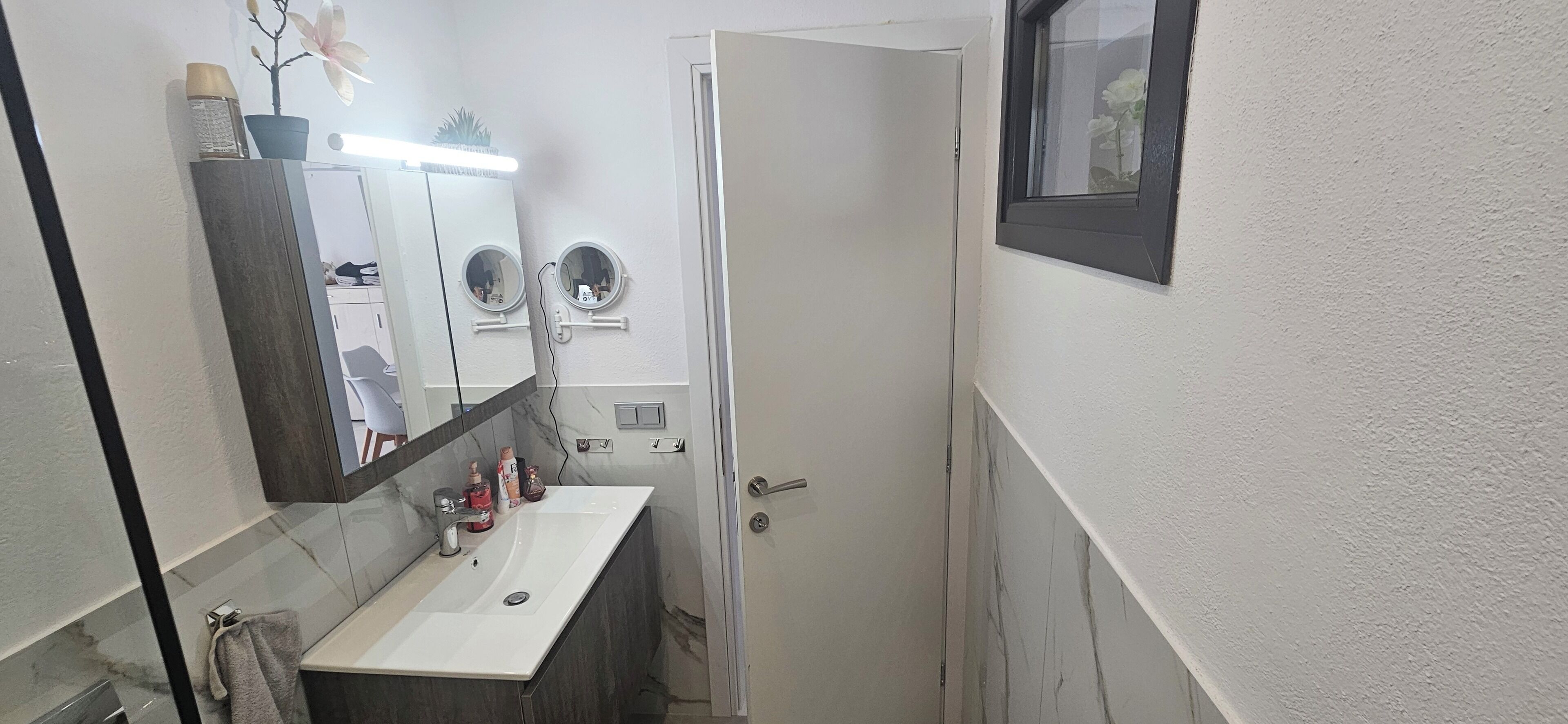 A bathroom with a white sink, two round mirrors, a towel rack, and a door.