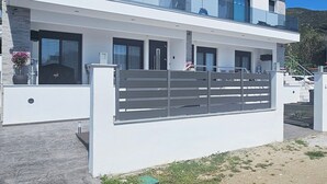 Ett modernt hus i två våningar med stora fönster, en balkong och en grind vid infarten.