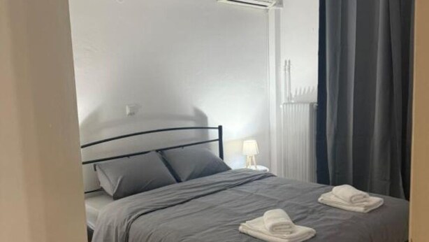 A neatly made bed with grey bedding and two folded towels on the footboard.