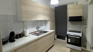 A modern kitchen with light wood cabinets, a white countertop, a sink, a stove, and a hanging light fixture.