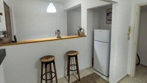 A compact kitchen with a white refrigerator, a wooden countertop, two stools, and a hanging pendant light.