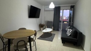 A modern living room with a dining table, sofa, and a flat-screen TV mounted on the wall.