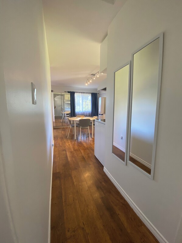 A hallway with wooden flooring, white walls, and a dining area with a table and chairs.