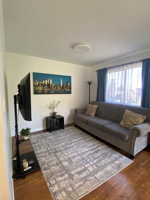 A living room with a grey sofa, a painting of a cityscape, a floor lamp, and a TV on a stand.