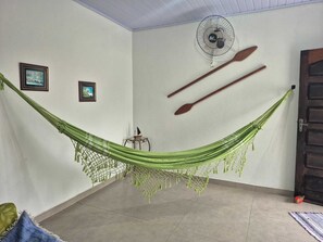 A room with a hammock, two wooden paddles, a fan, and two framed pictures on the wall. - Porto Velho Retreat (Ilha Comprida)