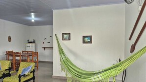 Una habitación con una hamaca verde, sillas de madera, una mesita y dos cuadros en la pared.