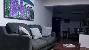 Un saló amb un sofà gris, una taula de centre i un quadre amb flors morades a la paret.