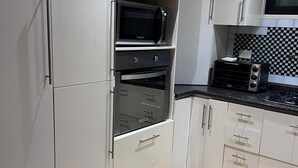 Una cuina amb armaris blancs, un microones, un forn i una torradora.