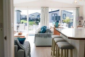A modern living room with a sofa, a dining table, and a bar area. - Luxury Hot Tub Lodge - Highcliffe Meadow (Barton on Sea)