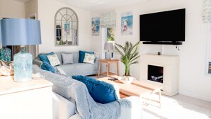 Un salon moderne avec un canapé d’angle, un téléviseur à écran plat, une cheminée et une grande fenêtre.
