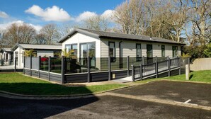 Une caravane moderne dotée d’un espace extérieur couvert, d’un jardin clôturé et d’une allée pavée.