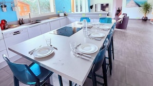 Een moderne keuken met een centraal eiland, blauwe stoelen en een eettafel voor vier personen.