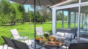 Een terras met zitplaatsen buiten, een tafel met ontbijtartikelen en uitzicht op een groen landschap.