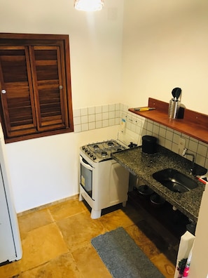 A compact kitchen with a gas stove, a sink, and a window with wooden shutters.