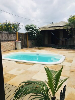 A rectangular swimming pool with a tiled deck, surrounded by a brick wall and a wooden fence.