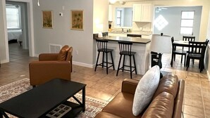 Een moderne woonkamer met een bruine leren bank, een zwarte salontafel, en een eethoek met een klein schiereiland en barkrukken.