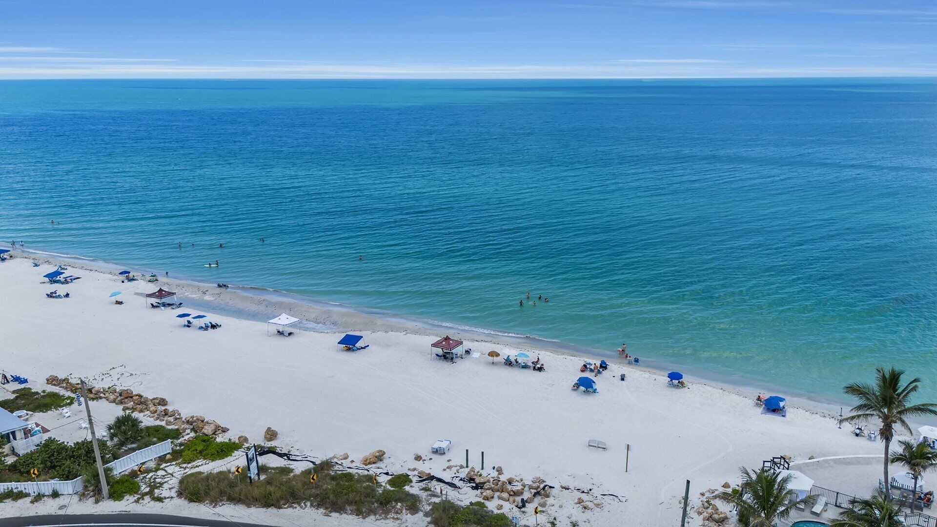 A beach with clear blue water, white sand, and several umbrellas and lounge chairs.
