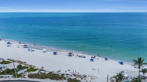 Een strand met helderblauw water, wit zand en diverse parasols en ligbedden.