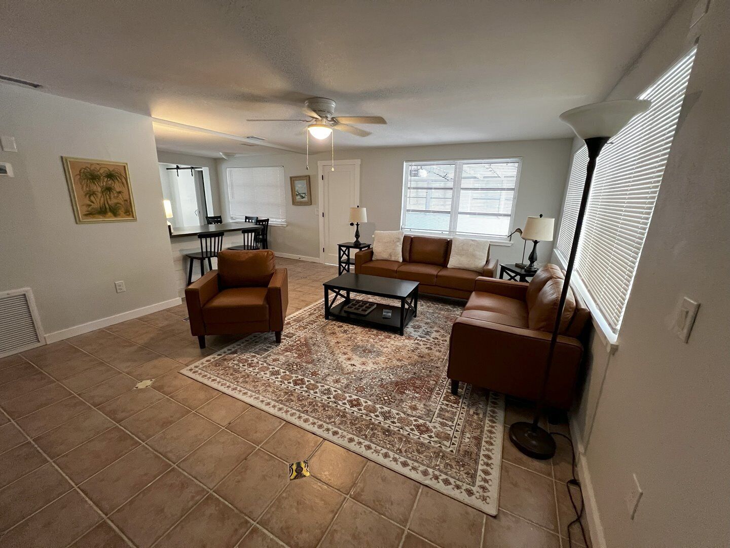 A living room with a ceiling fan, a brown leather sofa, a coffee table, and a patterned rug.