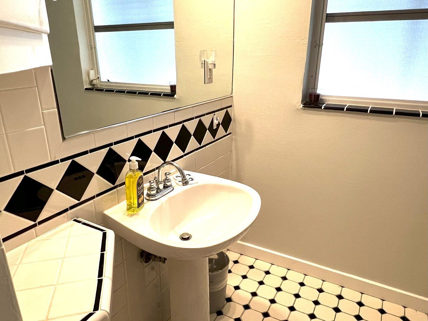 Un baño con un lavamanos blanco, un espejo encima y una ventana.