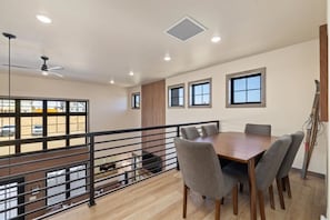 A dining area with a wooden table and grey chairs, a balcony with a metal railing, and a view of a parking lot. - Luxury Family Getaway / Private Hot tub (Red Lodge)