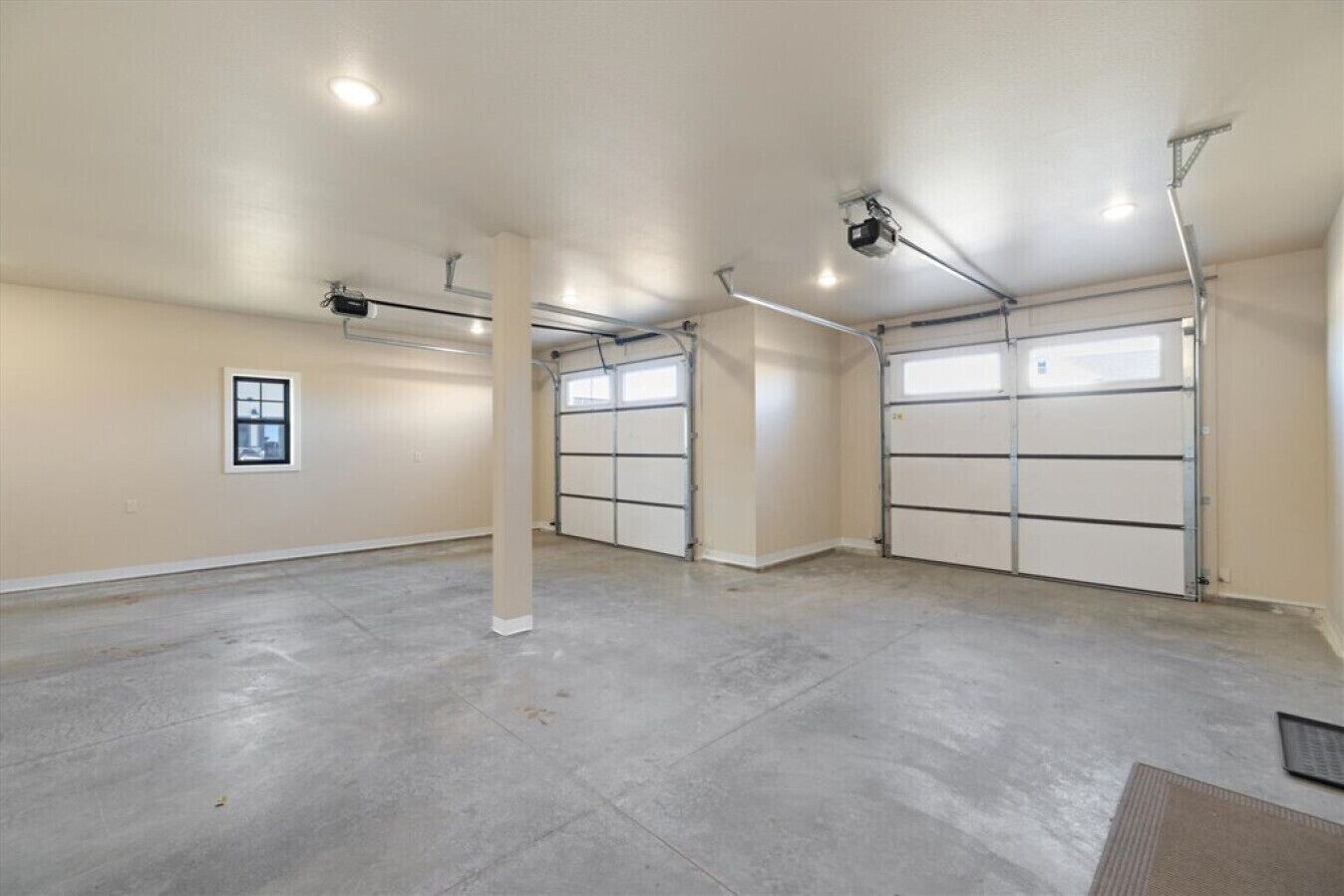 A spacious garage with three large garage doors, a concrete floor, and a single window on the left wall.