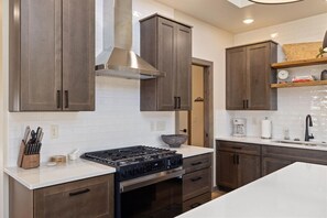 A modern kitchen with dark wooden cabinets, a stainless steel range hood, and a white countertop. - Luxury Family Getaway / Private Hot tub (Red Lodge)