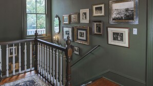 Un escalier avec une rampe en bois et des balustrades blanches, menant à un palier dont le mur est peint en vert foncé et orné de photographies en noir et blanc encadrées.