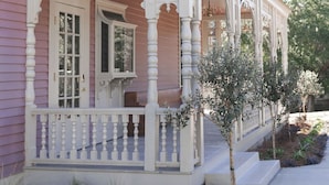 Een roze huis met een witte veranda en een kleine boom ervoor.