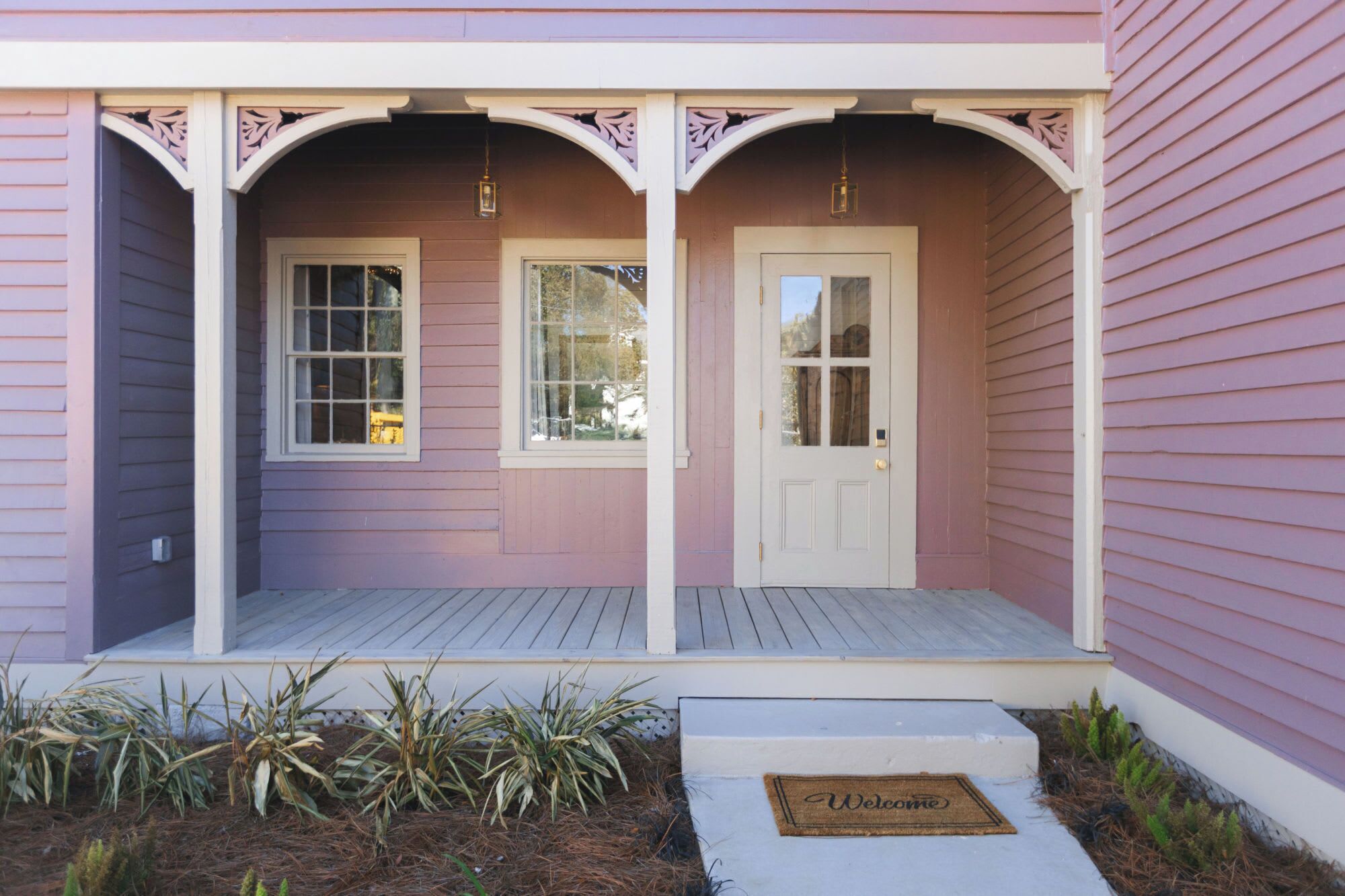 A house with a porch, two windows, a door, and a welcome mat.