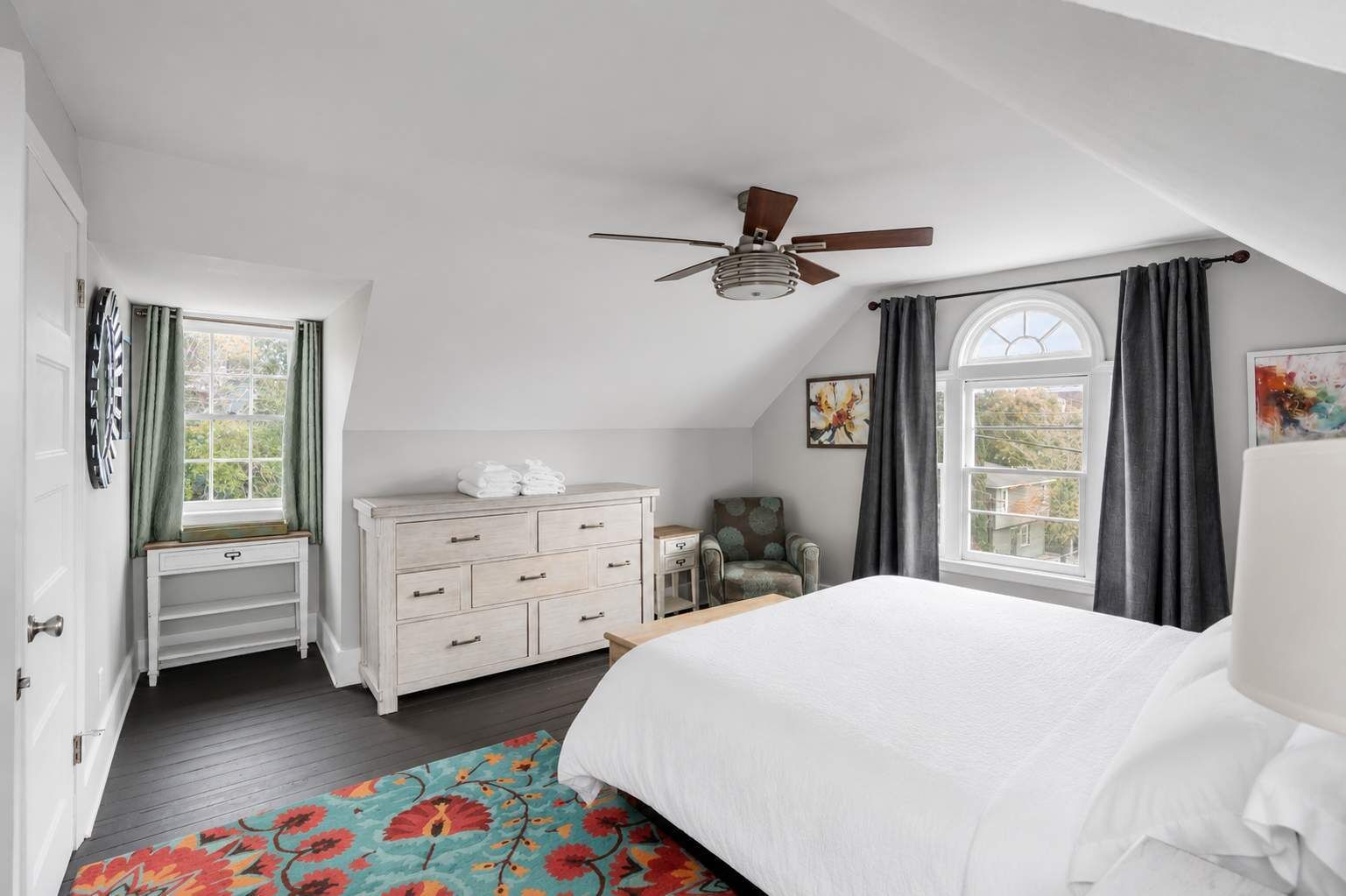Une chambre à coucher comprenant un lit, une commode, une chaise, une fenêtre et un ventilateur de plafond.